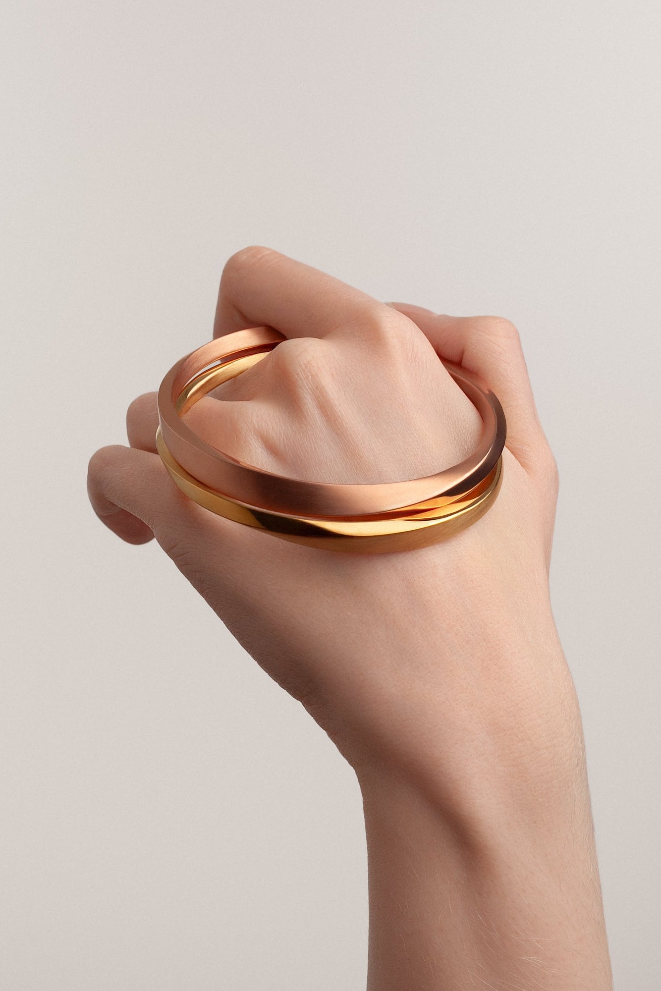 Hand holding a gold bracelet against a neutral background